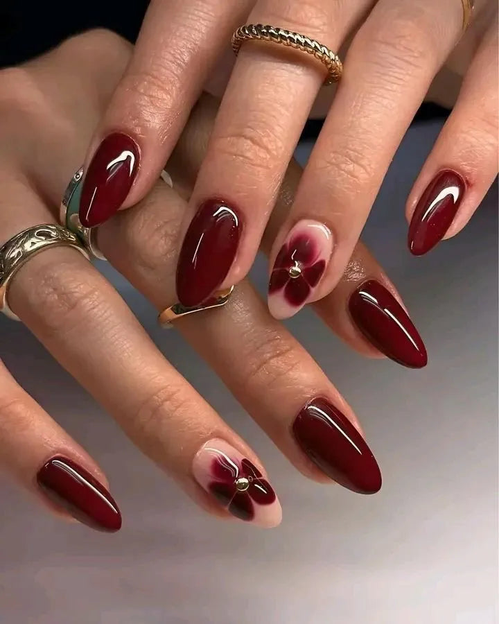 Close-up of hands with burgundy nail polish and floral designs on a neutral background